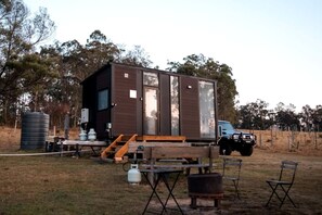 A small cabin with a ramp leading to the door, a table with chairs, and a blue truck parked nearby.