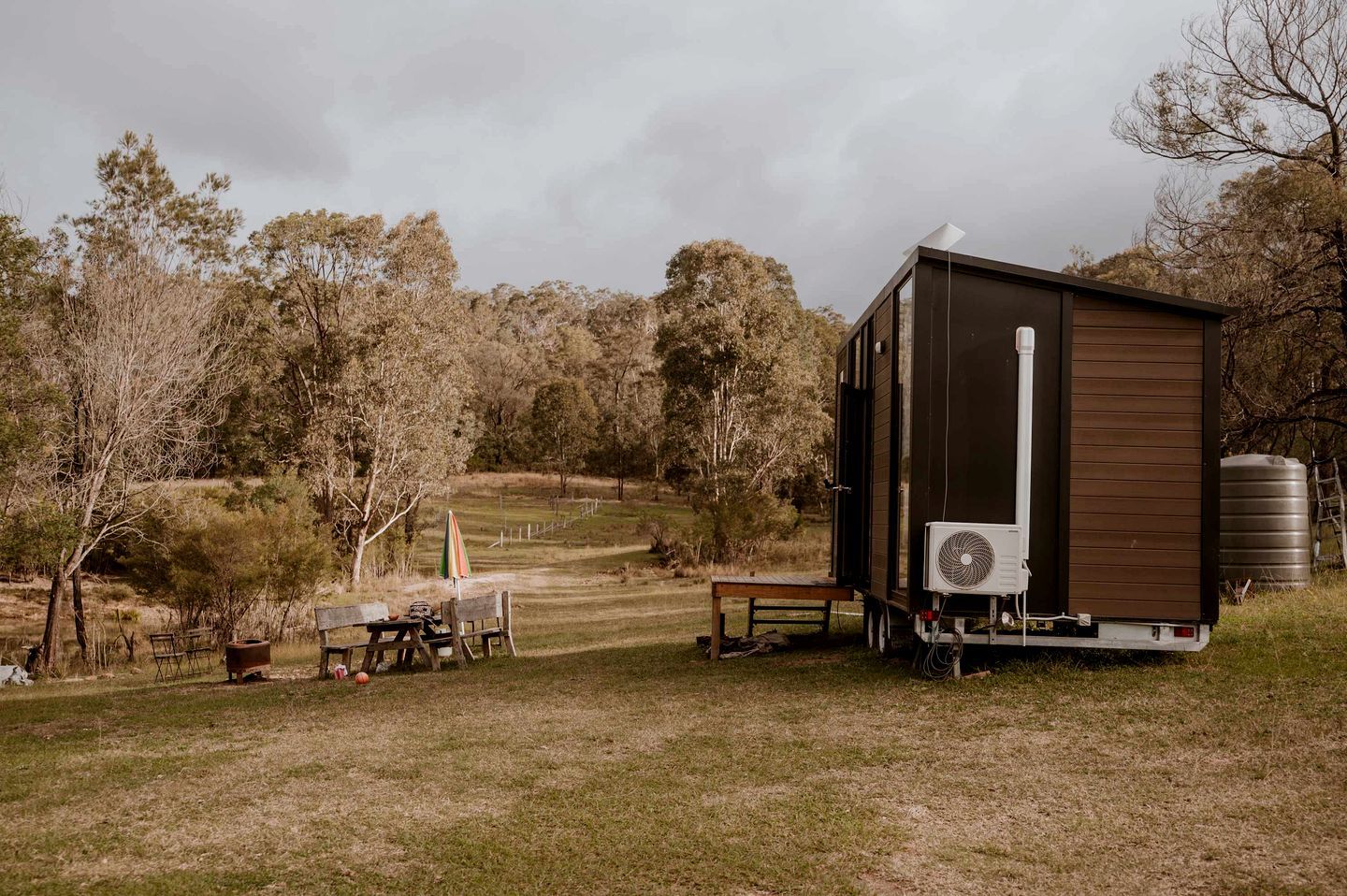 Een moderne stacaravan met een grote ventilator, een watertank en een picknicktafel, gelegen in een landelijke omgeving.