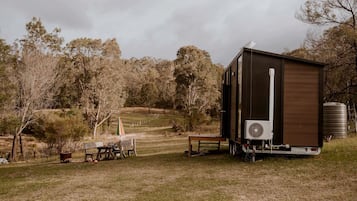 Een moderne stacaravan met een grote ventilator, een watertank en een picknicktafel, gelegen in een landelijke omgeving.