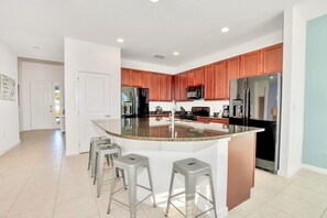 A modern kitchen with a central island, stainless steel appliances, and wooden cabinets. - Waterfront Family Mansion w BBQ, Games Room & Pool (Kissimmee)