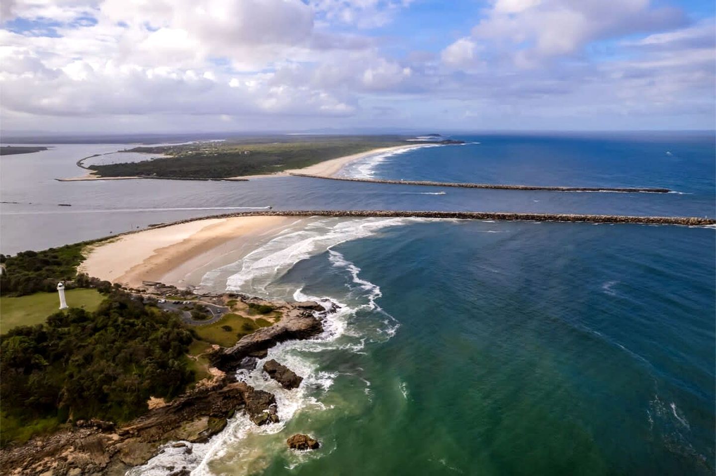 Vista aérea de una zona costera con una playa, un faro y un rompeolas.