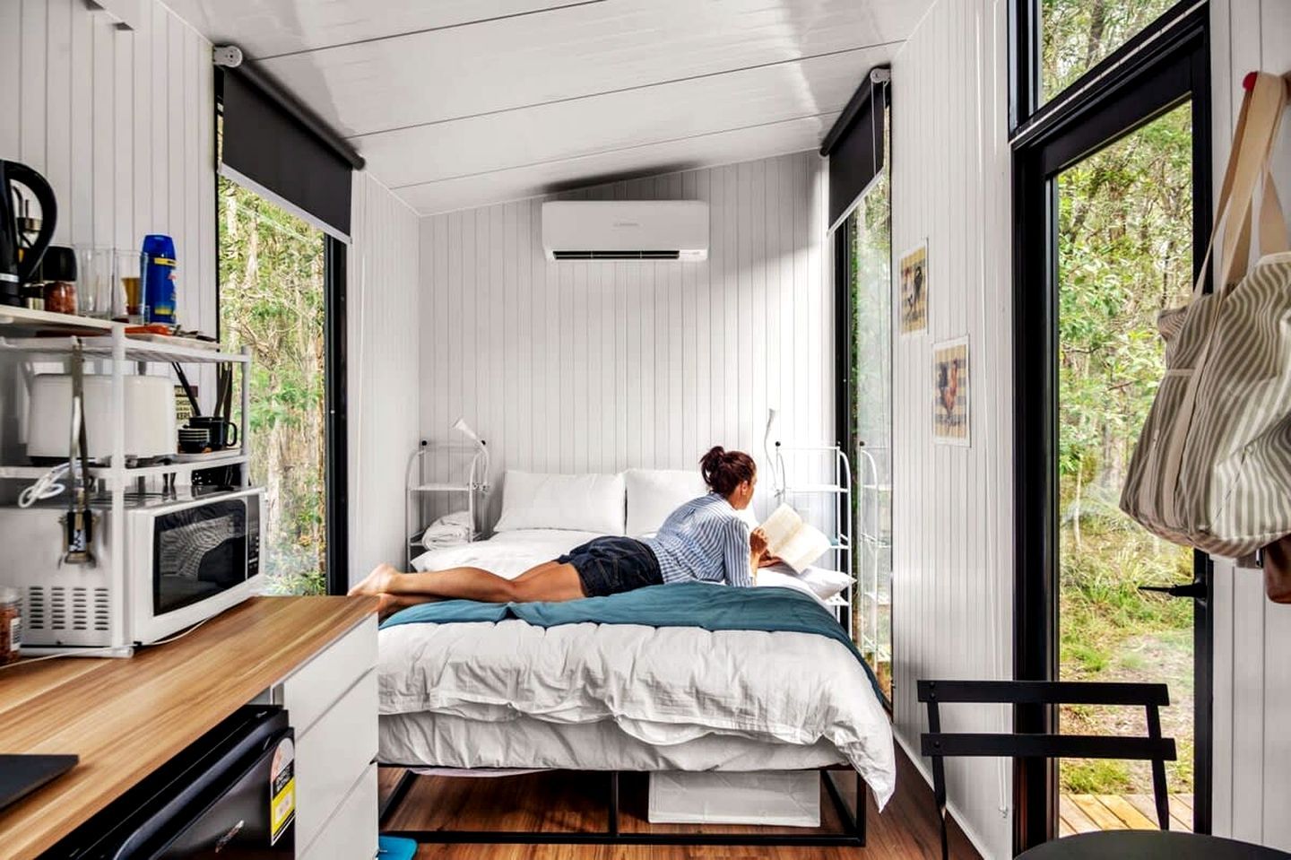 Un dormitorio compacto con cama, una butaca para leer y una pequeña cocina.