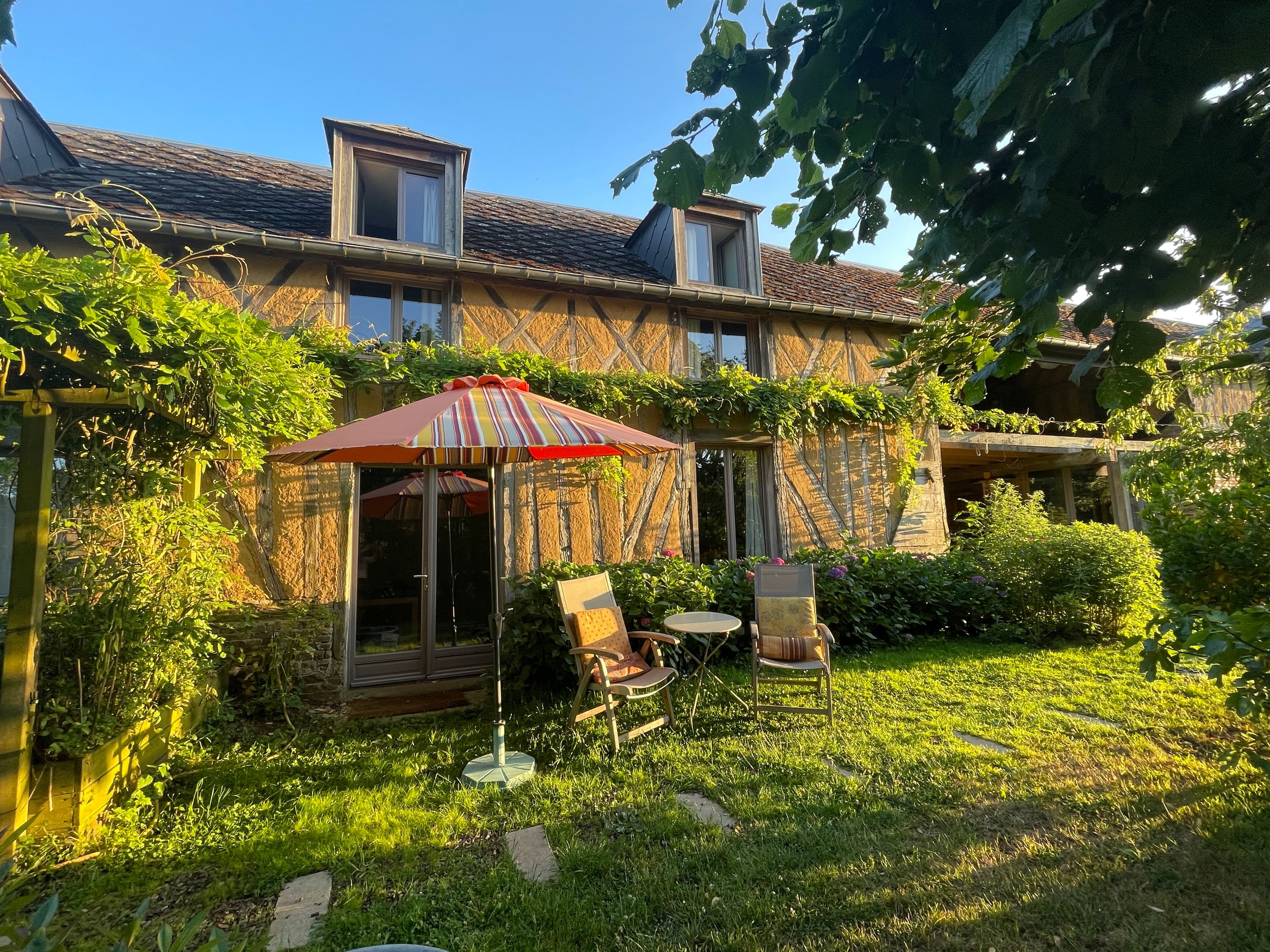 Een huis met een tuin, een terras met stoelen en een gestreepte parasol.