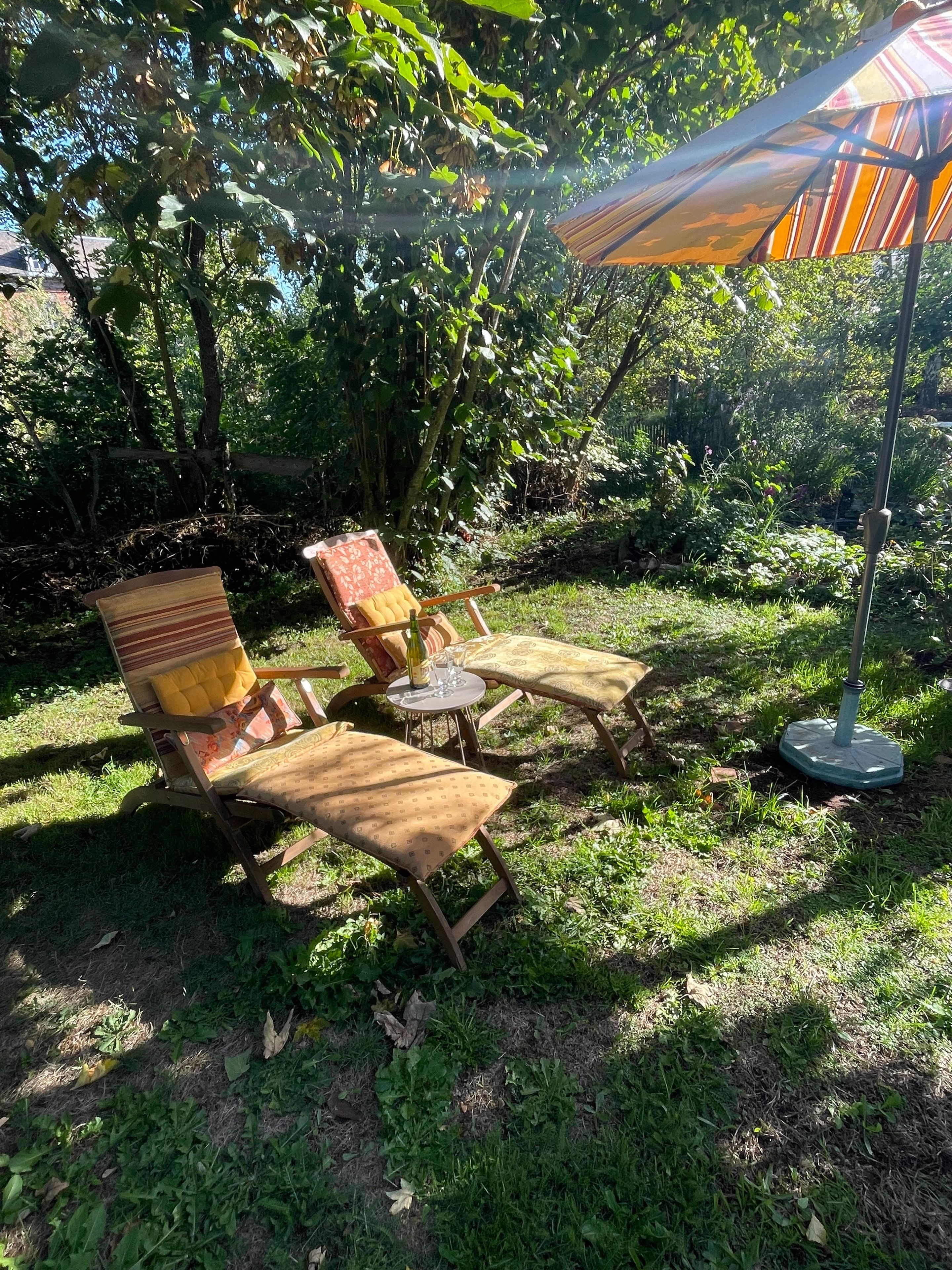 Un área de estar al aire libre con dos sillas de madera y una mesa, rodeada de exuberante follaje.