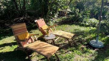 Un área de estar al aire libre con dos sillas de madera y una mesa, rodeada de exuberante follaje.