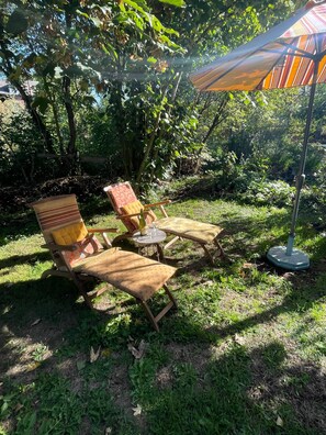 Un área de estar al aire libre con dos sillas de madera y una mesa, rodeada de exuberante follaje.