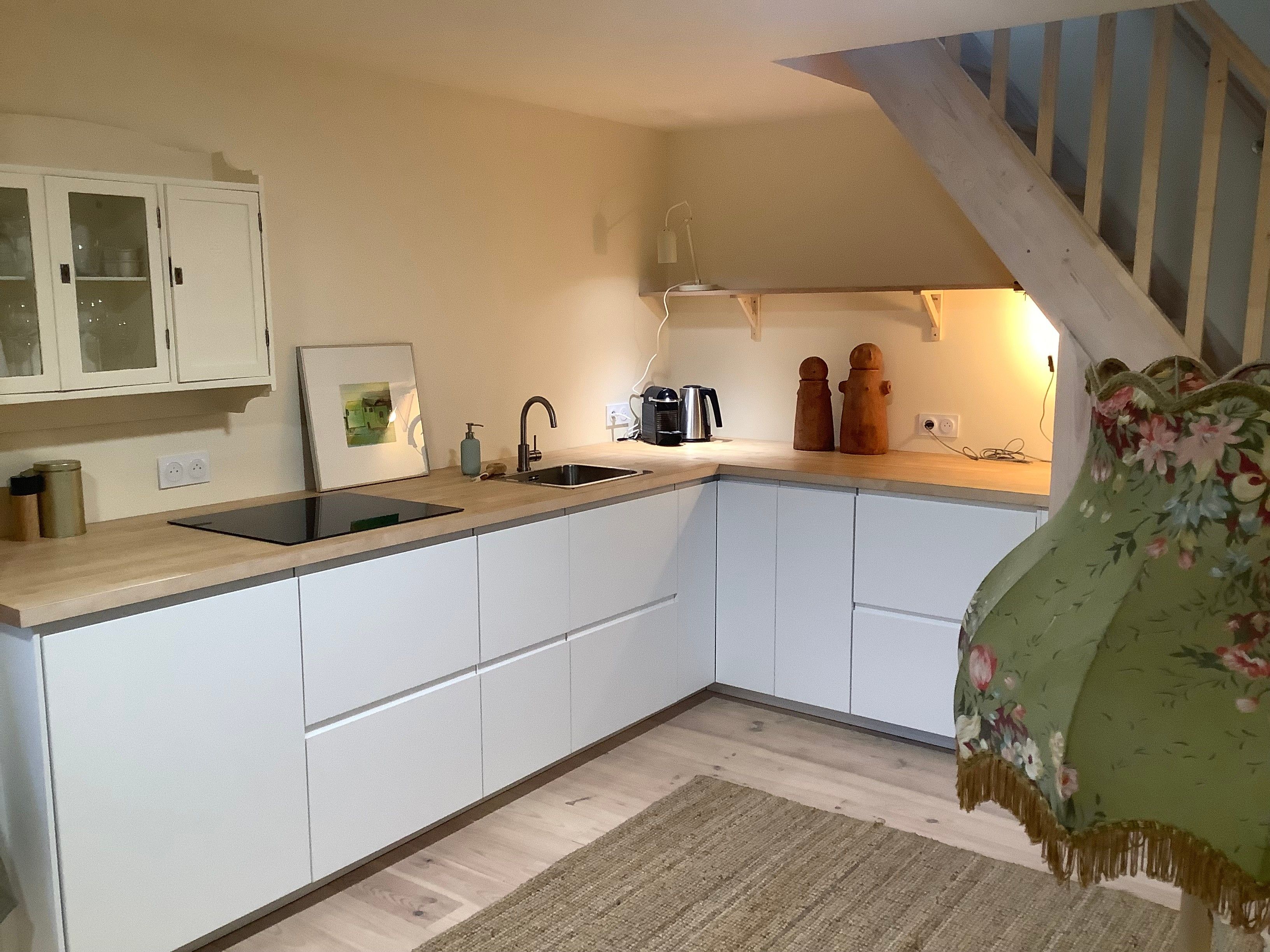 A kitchen with white cabinets, a black sink, a coffee maker, and a wooden staircase.