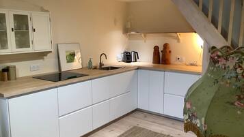 A kitchen with white cabinets, a black sink, a coffee maker, and a wooden staircase.