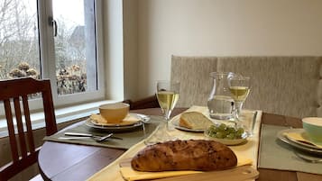 A dining table with a loaf of bread, a bowl of grapes, and glasses of white wine.