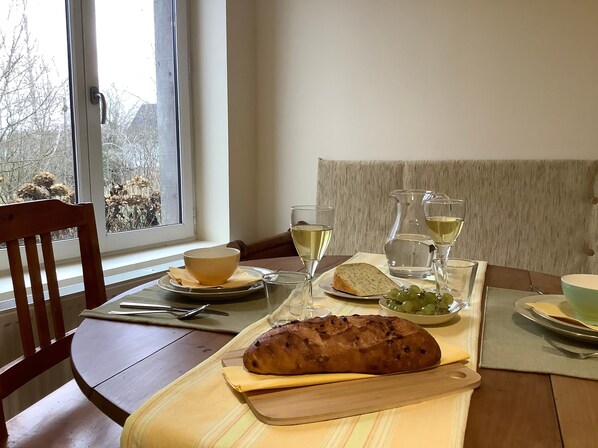 A dining table with a loaf of bread, a bowl of grapes, and glasses of white wine.
