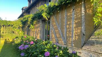 Un edificio con fachada de entramado tradicional, un jardín con flores de hortensia y un cielo azul despejado.
