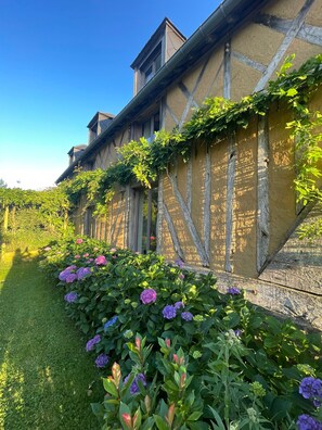 Un edificio con fachada de entramado tradicional, un jardín con flores de hortensia y un cielo azul despejado.