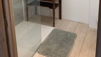 Un baño con tragaluz, cabina de ducha de vidrio, una mesa de madera con una toalla y un panel de pared con ganchos.