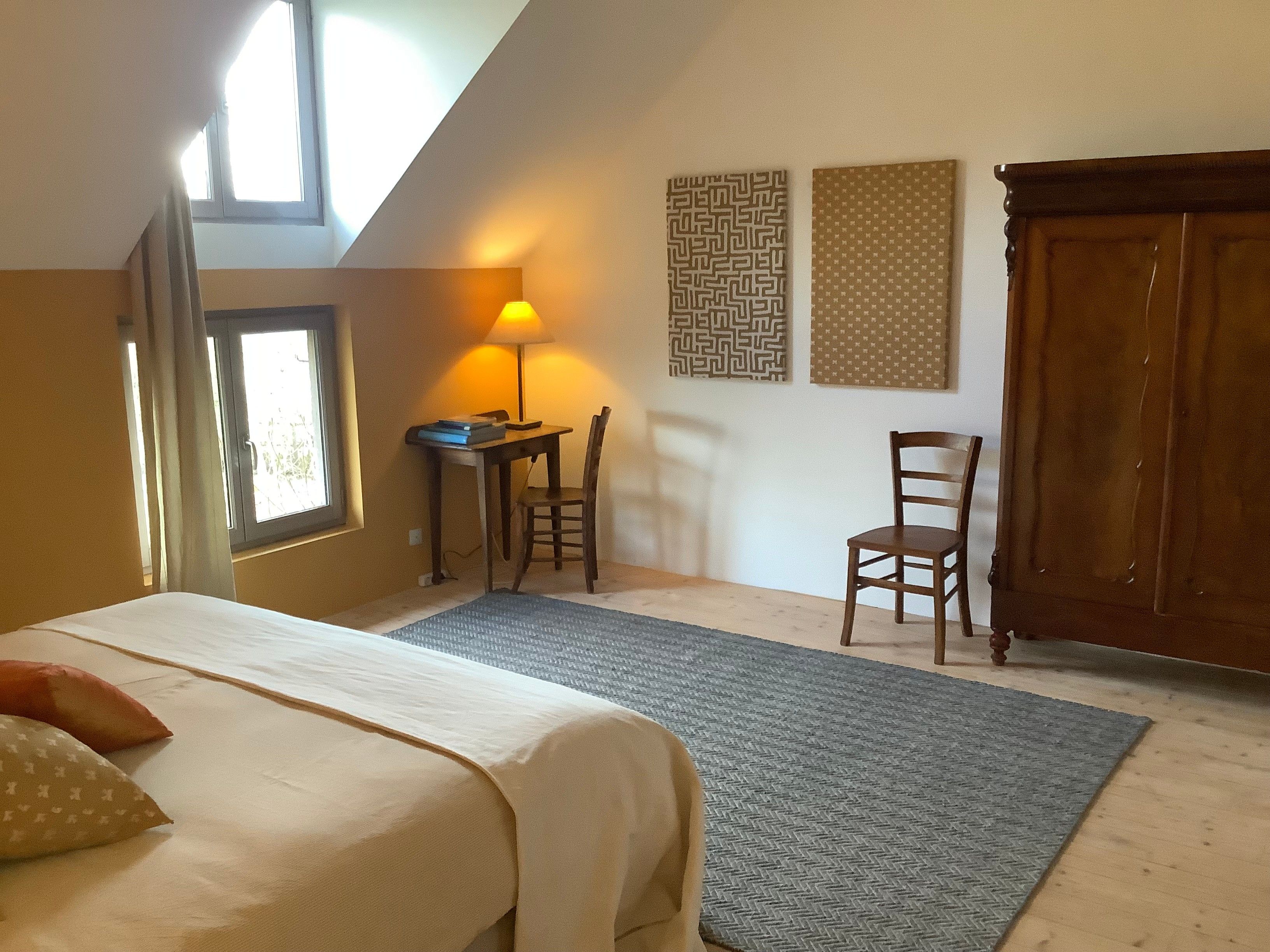 Een slaapkamer met een bed, bureau, twee stoelen, een lamp en een raam.