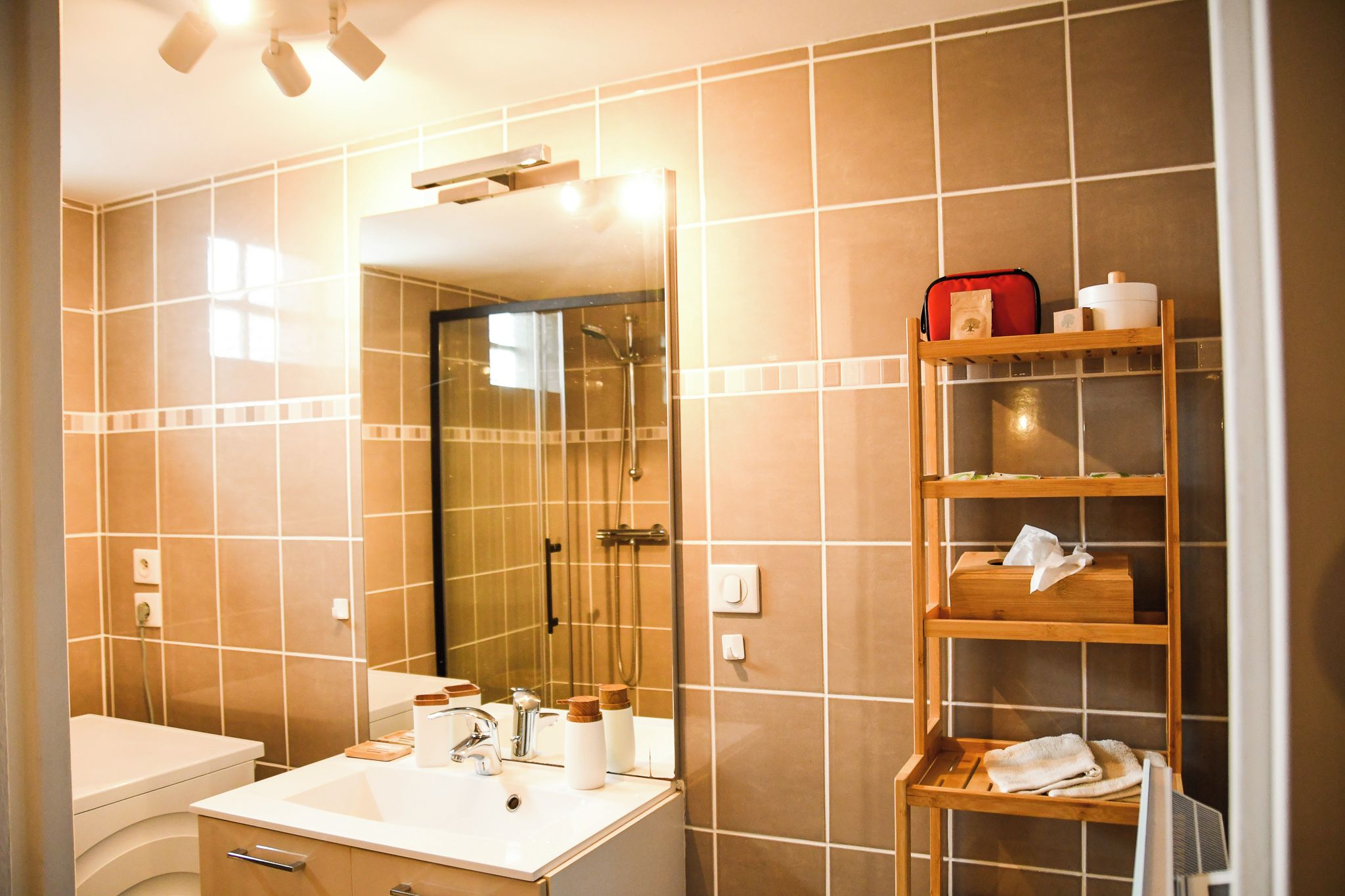 Ein Badezimmer mit einem weißen Waschbecken, einem Spiegel und einem Holzregal mit Toilettenartikeln.