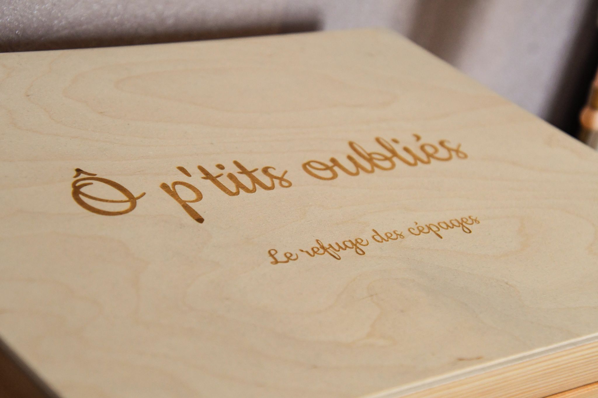 Une boîte en bois avec le texte en relief : « O p’tits oüblies, le refuge des cépages ».