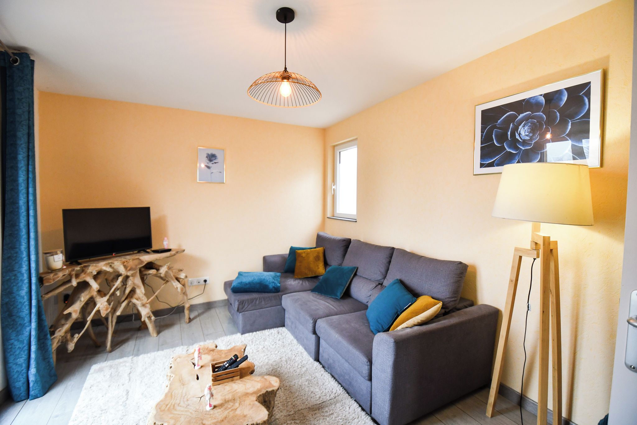 Un salon avec un canapé, un téléviseur, une table basse en bois, une lampe et un tableau accroché au mur.