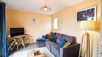 Un salon avec un canapé, un téléviseur, une table basse en bois, une lampe et un tableau accroché au mur.