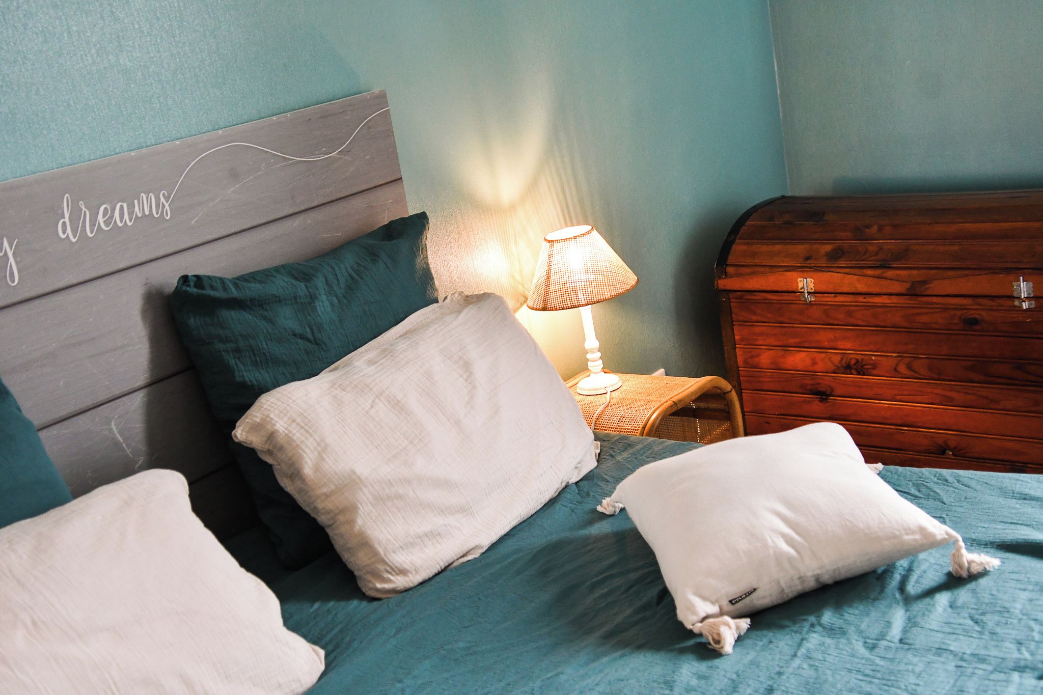 Ein Schlafzimmer mit einem Bett, Kissen, einem Nachttisch, einer Lampe und einer Holzkommode.