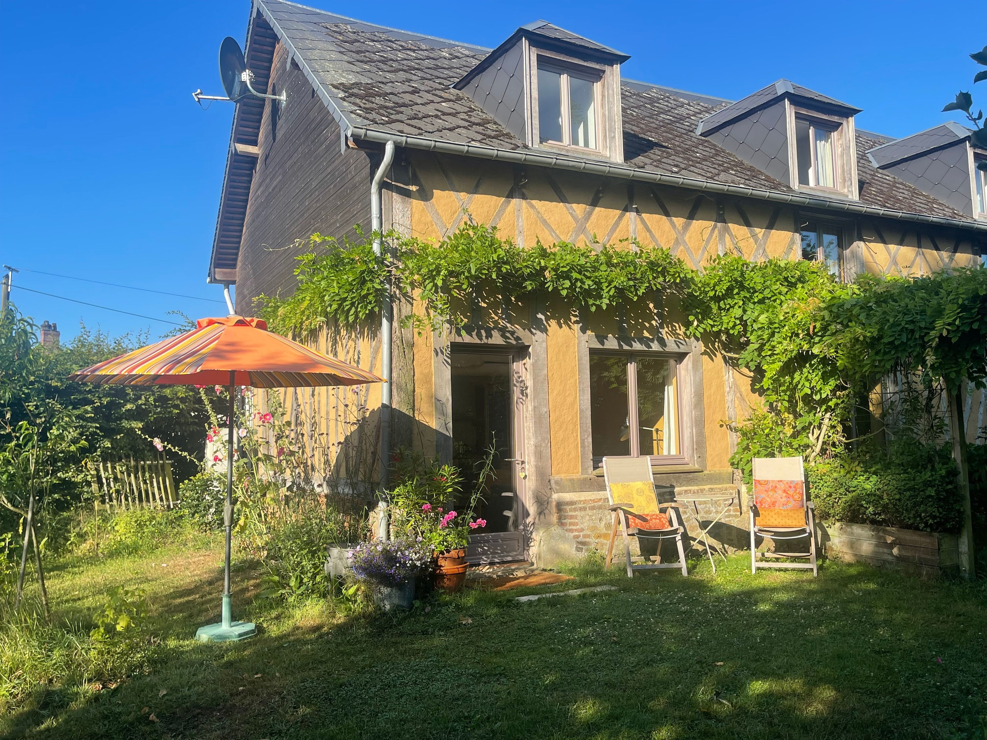 Ein Haus mit einem geneigten Dach, einer Satellitenschüssel und einem Garten mit Stuhl und Sonnenschirm.