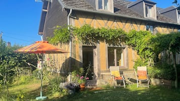 Ein Haus mit einem geneigten Dach, einer Satellitenschüssel und einem Garten mit Stuhl und Sonnenschirm.