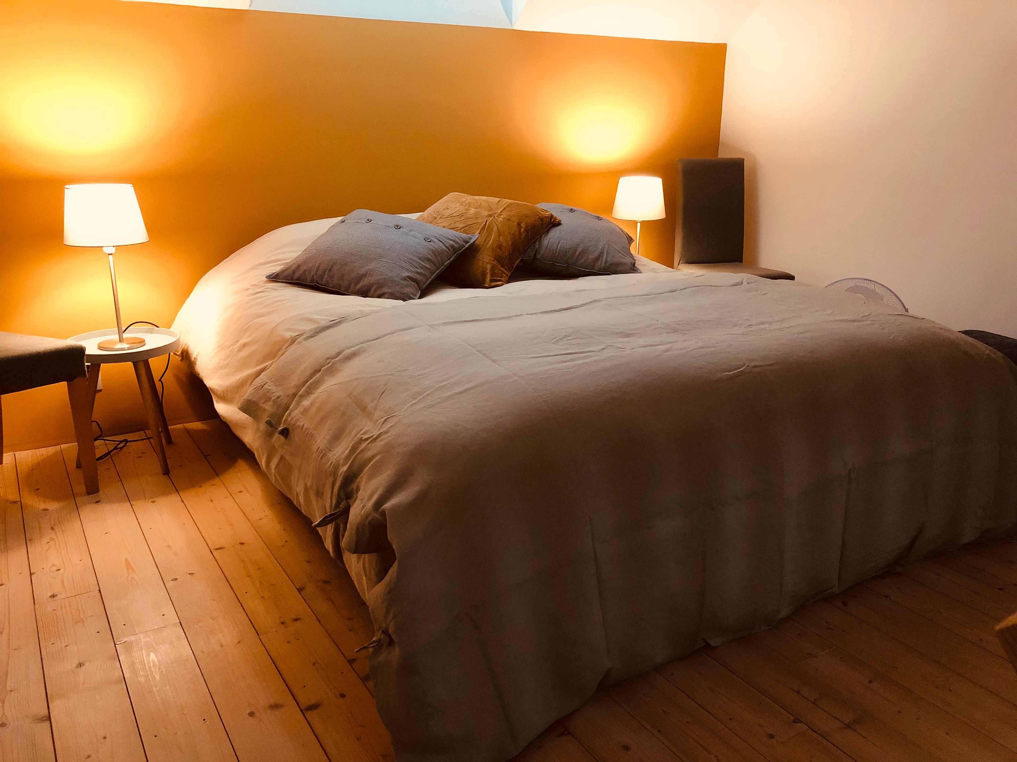 A bedroom with a large bed, two bedside lamps, and a wooden floor.