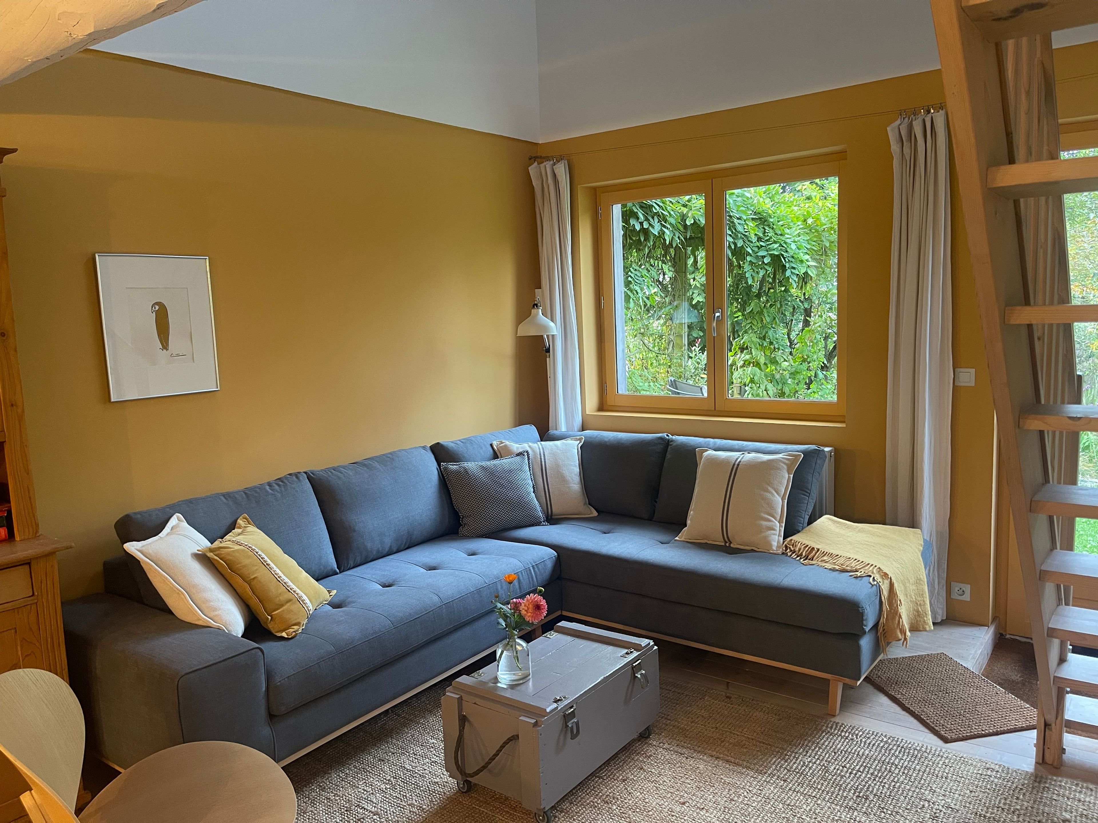 Ein Wohnzimmer mit einem blauen Sofa, einem kleinen Tisch mit einer Vase und einem Fenster mit Vorhängen.