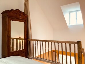 A room with a wooden bed, a mirror, a window, and a sloped ceiling.