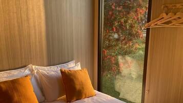 A hotel room with a large bed, pillows, towels, a window with a view of trees, and a wooden ceiling.