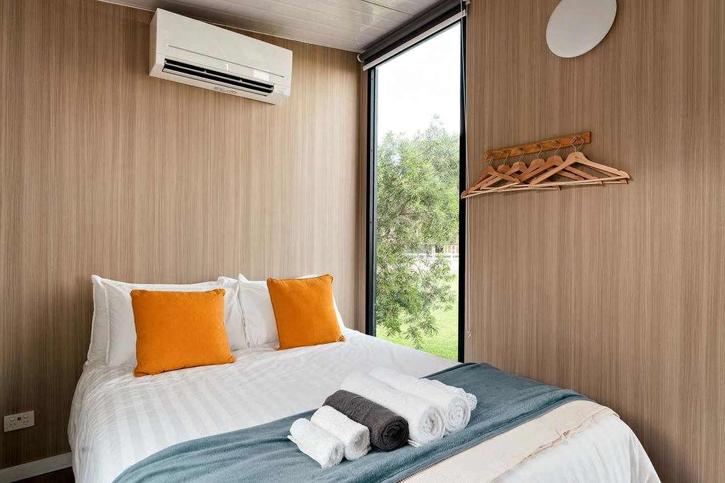 Een hotelkamer met een bed, een airconditioning, een raam met uitzicht op groen en een houten kapstok.