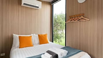 Een hotelkamer met een bed, een airconditioning, een raam met uitzicht op groen en een houten kapstok.