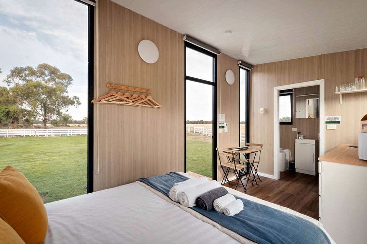 A modern hotel room with a large bed, a dining area, and a view of the outdoors.