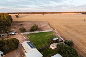 A large open field with a fenced area, a building with solar panels, and a small structure.