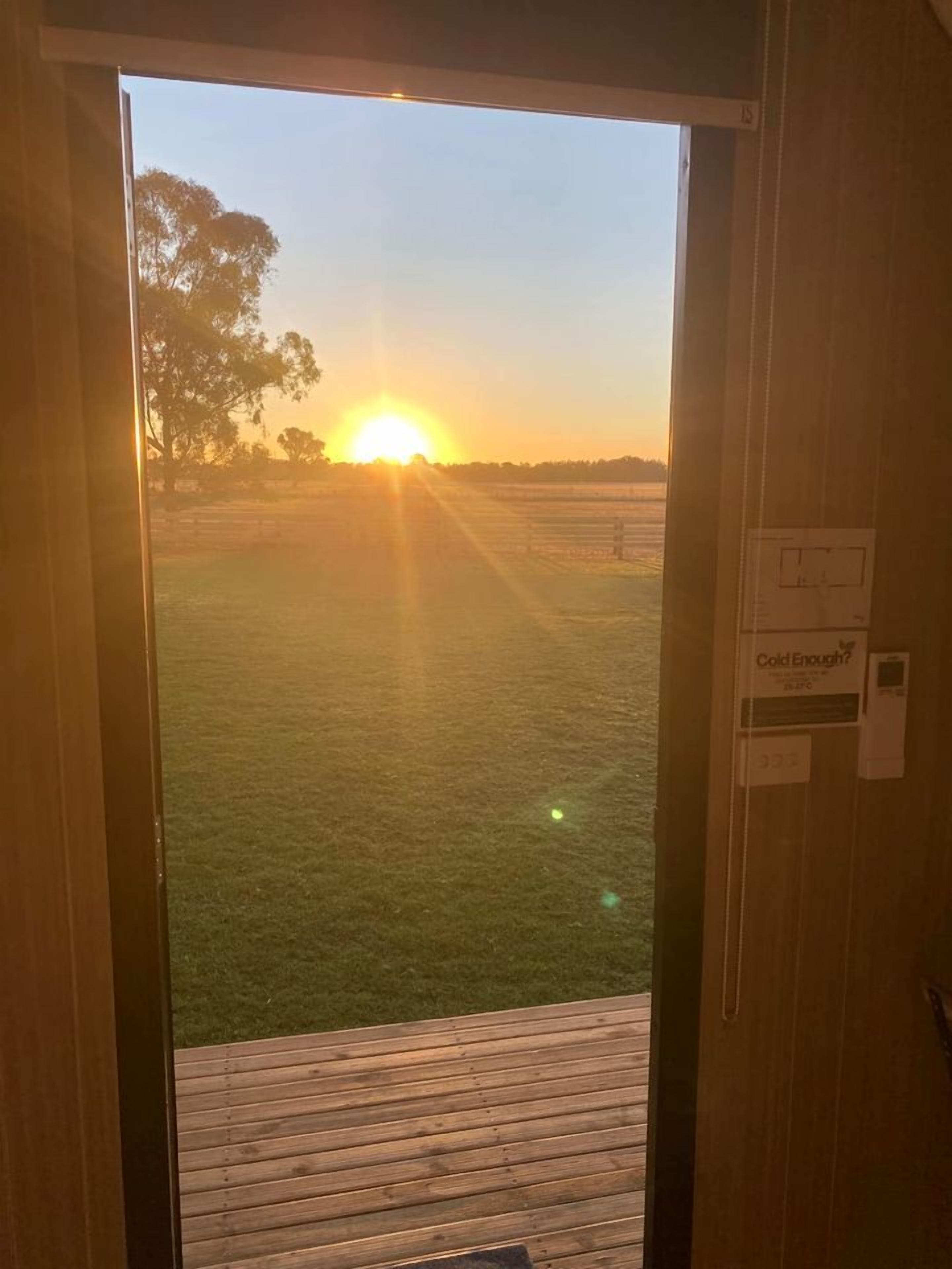 A doorway leading to a grassy outdoor area with a view of the sunset.
