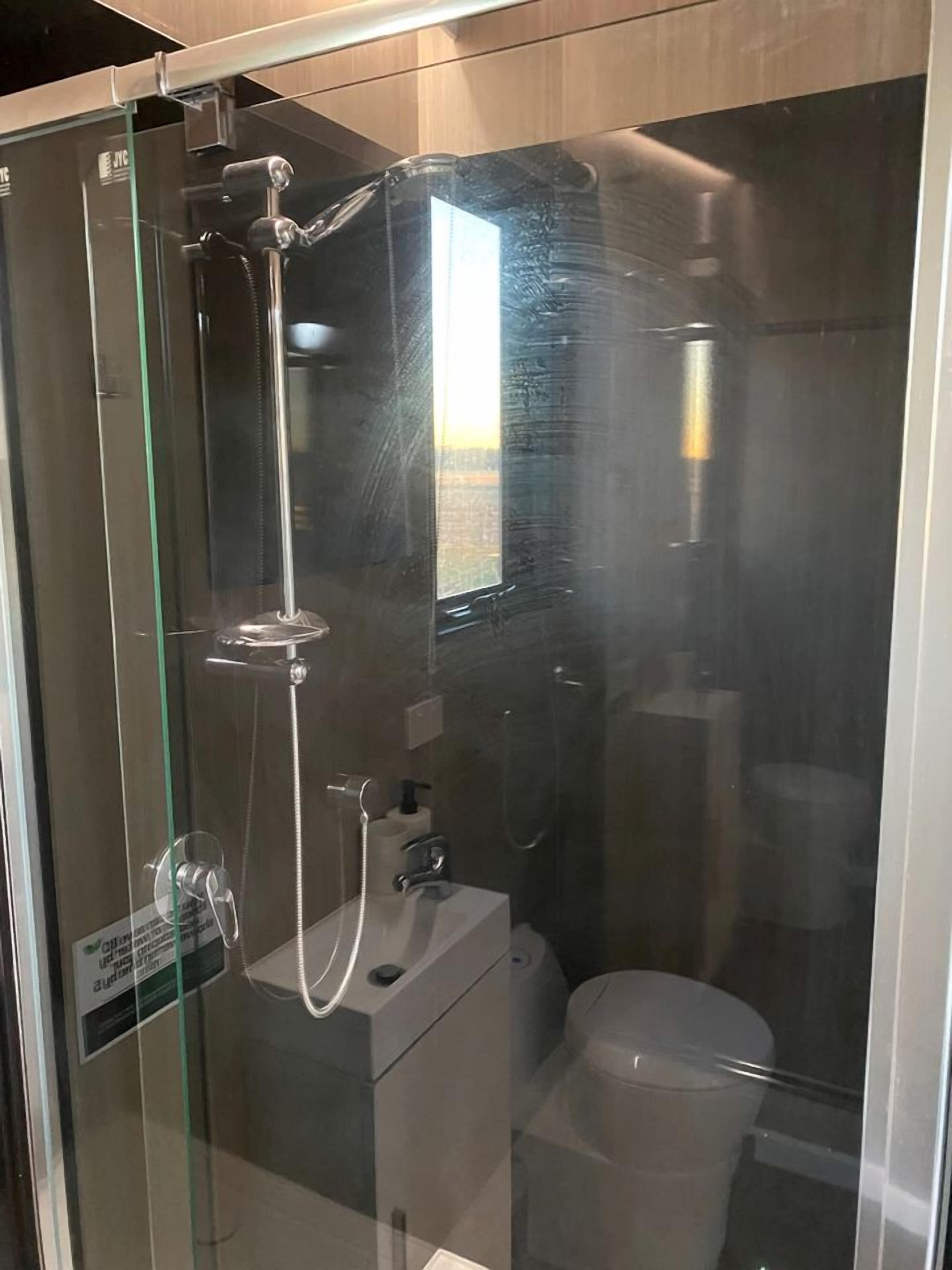 A glass-enclosed shower stall with a handheld showerhead, a handheld shower attachment, and a wall-mounted faucet.
