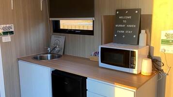 A compact kitchenette with a microwave, sink, and a sign that reads 'WELCOME TO MURRAY HAVEN FARM STAY.'