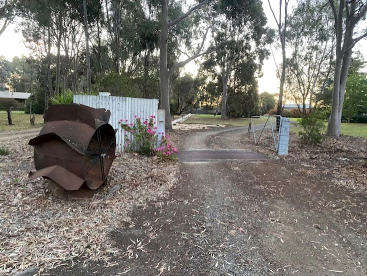 A dirt path leading to a gated area with a metal structure on the left and a fence with flowers in the background.