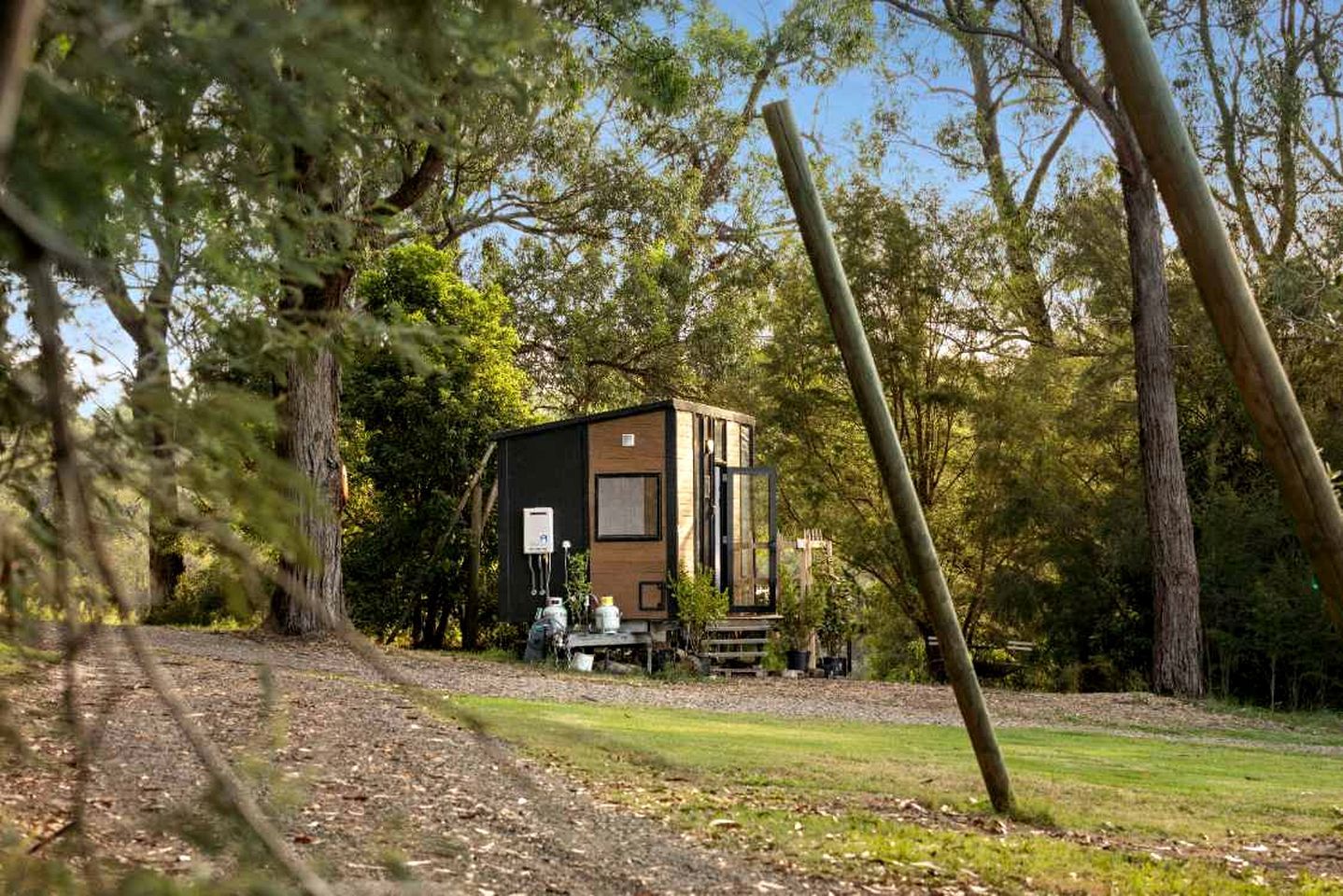 Een klein houten vakantiehuisje, omringd door bomen, met een bank ervoor.