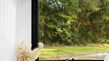 Una cocina con un lavamanos de acero inoxidable, un florero blanco con flores y una ventana con vistas a un paisaje verde.