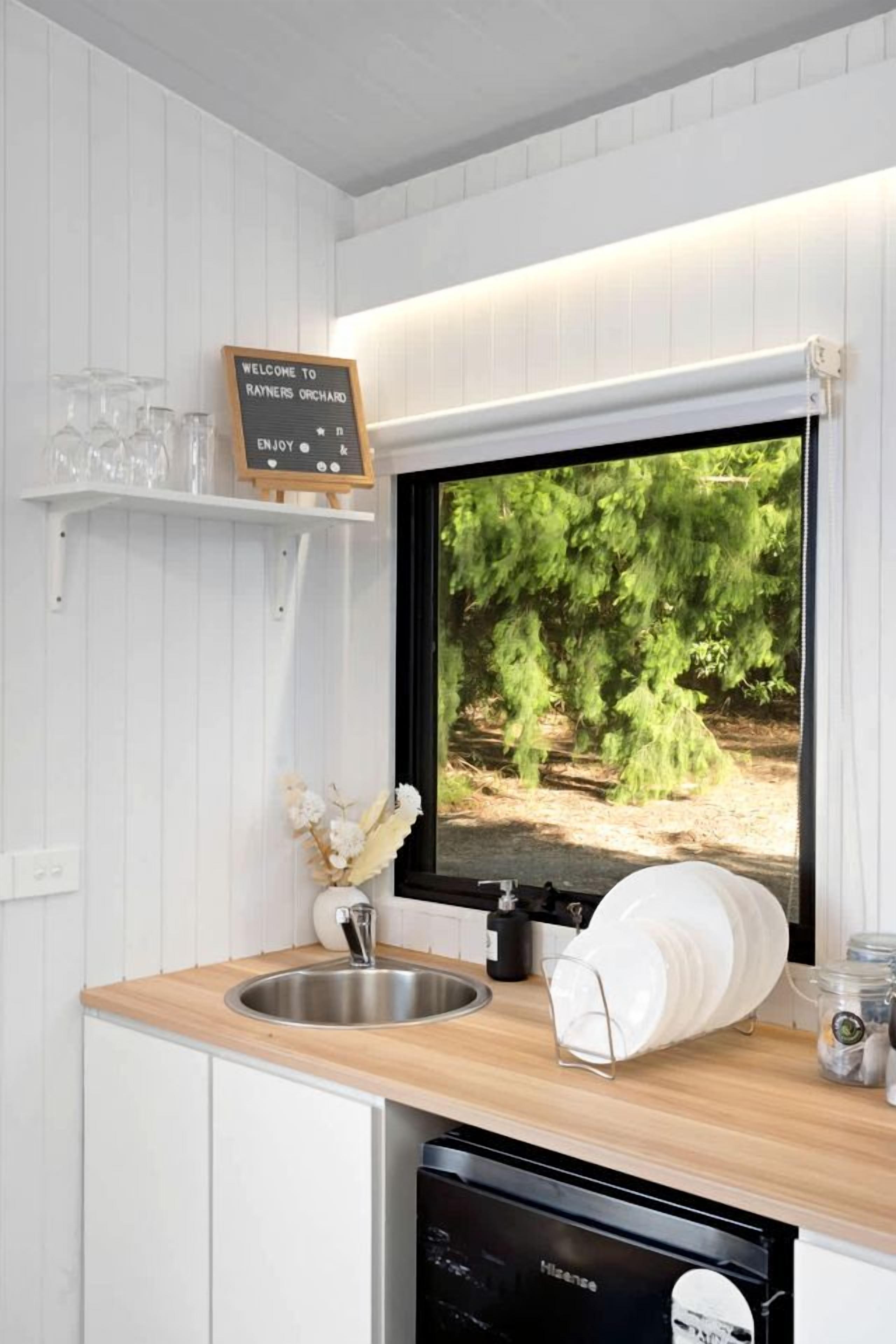 A kitchen with a built-in dishwasher, a sink, and a window displaying a forest scene.