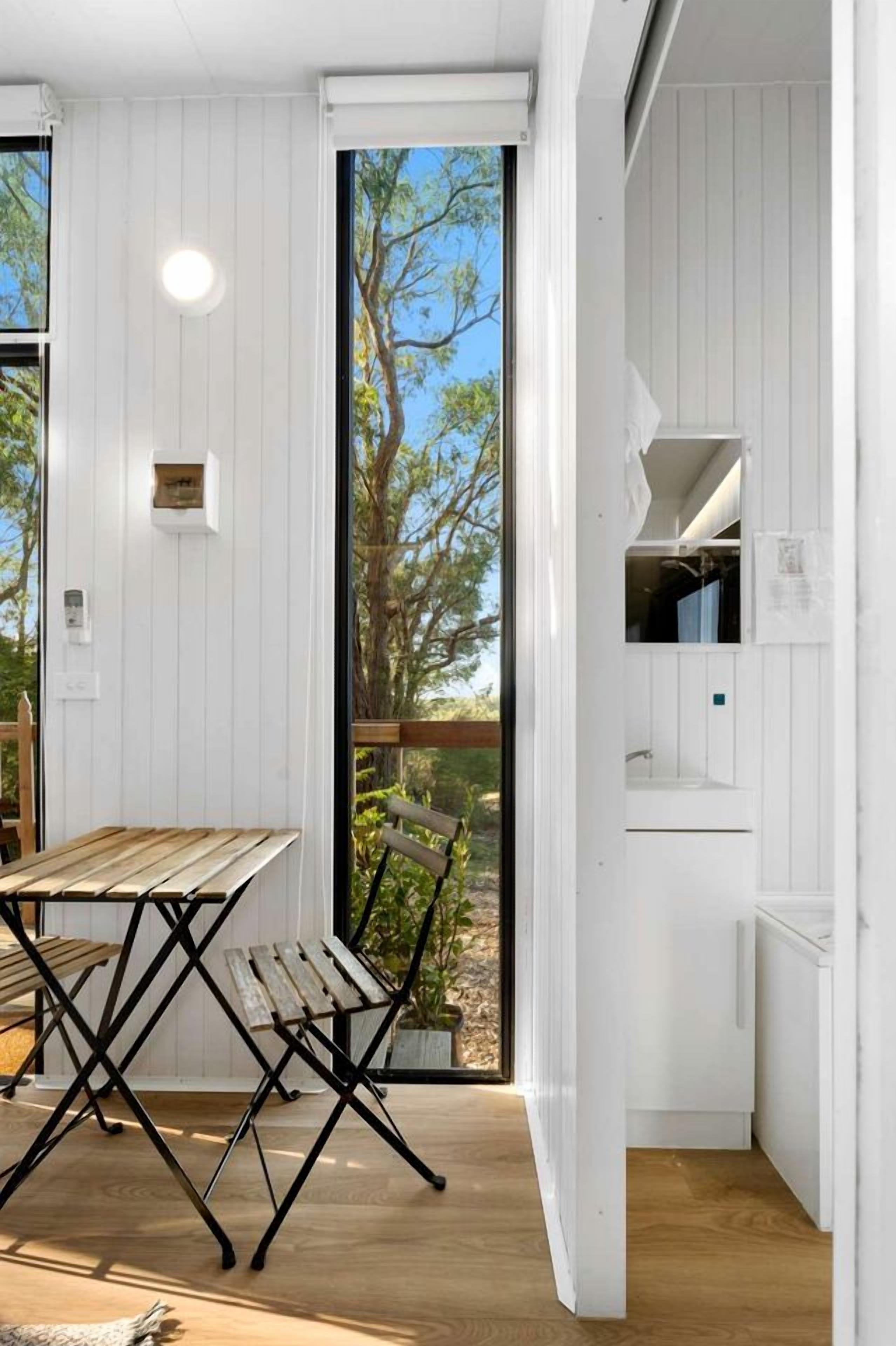 A room with a wooden table and chairs, a white wall with a window, and a view of trees.