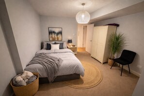 A bedroom with a bed, bedside table, lamp, wardrobe, chair, and a hanging light fixture. - Spacious 3BR Garden Retreat in Shepherd’s Bush (London)