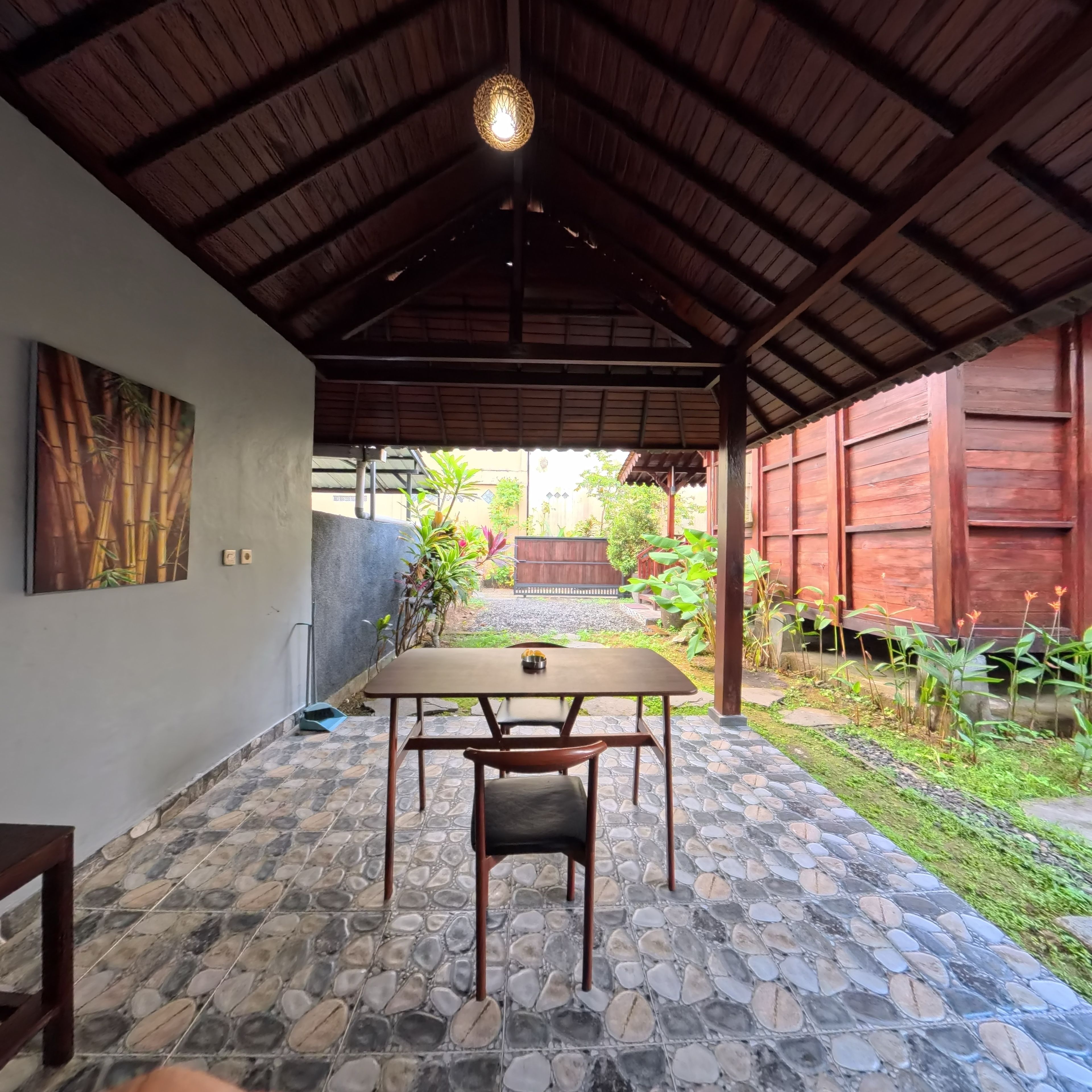 An outdoor covered patio with a table and chairs, a tiled floor, and a wooden ceiling.