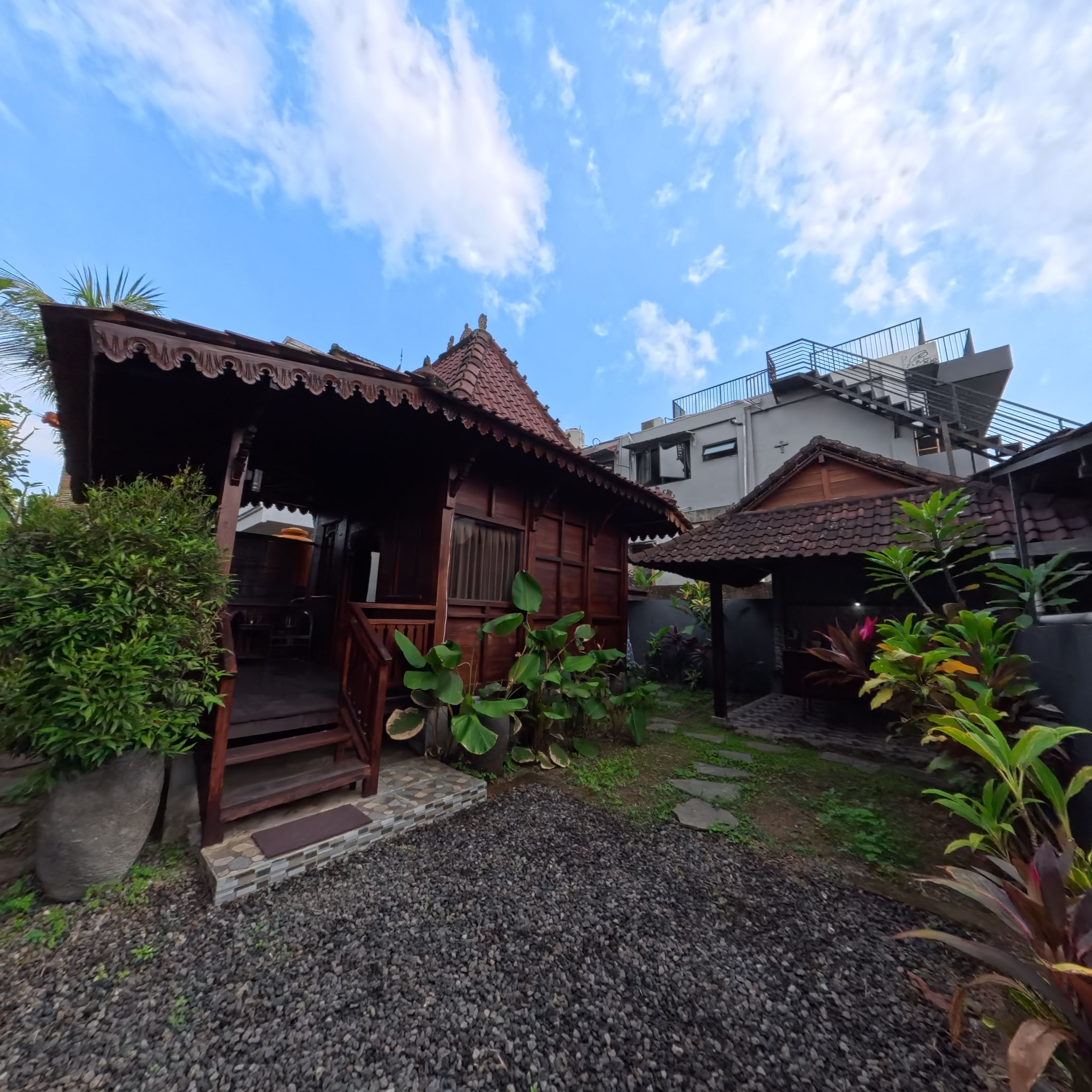 A traditional wooden house with a tiled roof, a porch, and a garden with gravel paths.