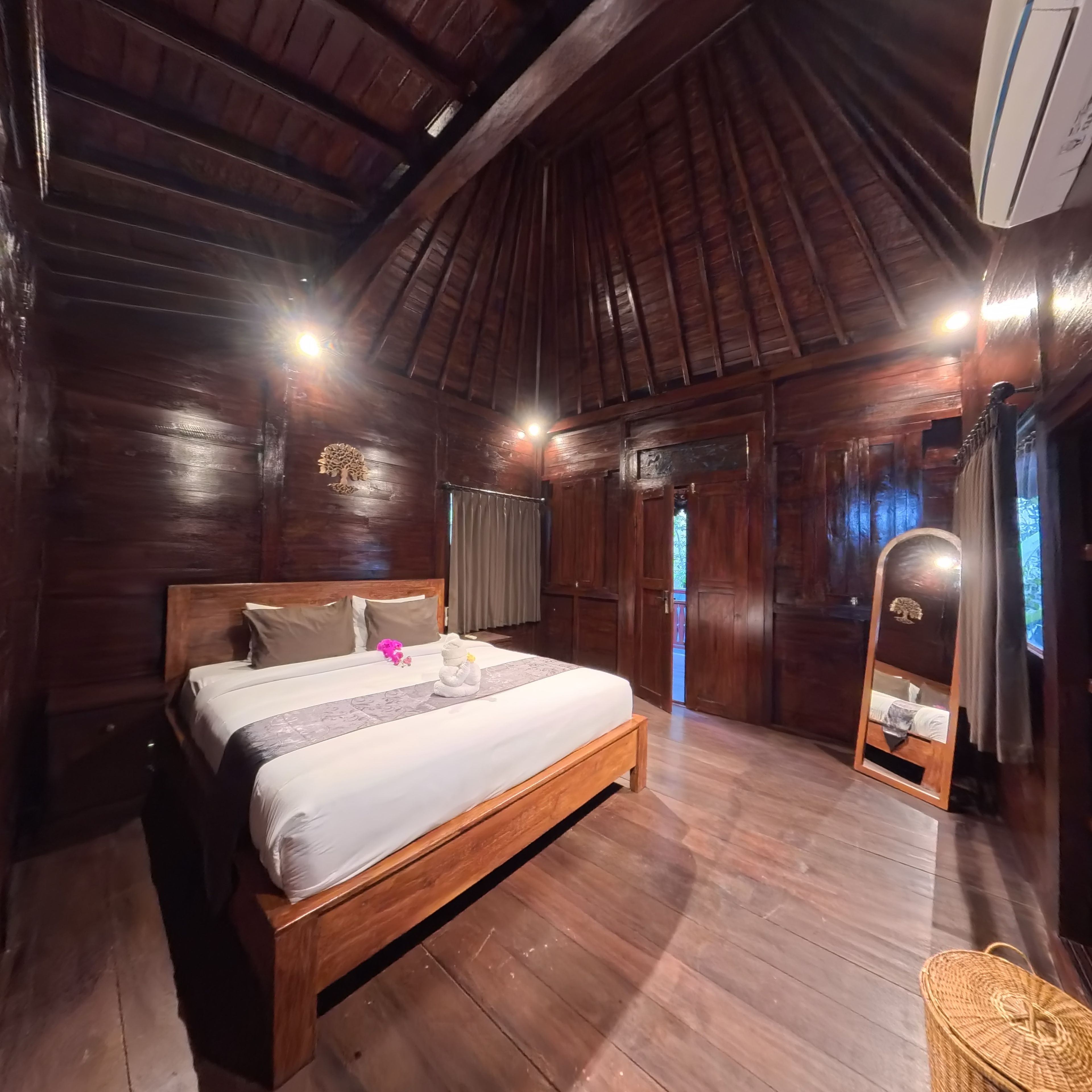 A wooden-paneled room with a large bed, a mirror, and a wooden floor.