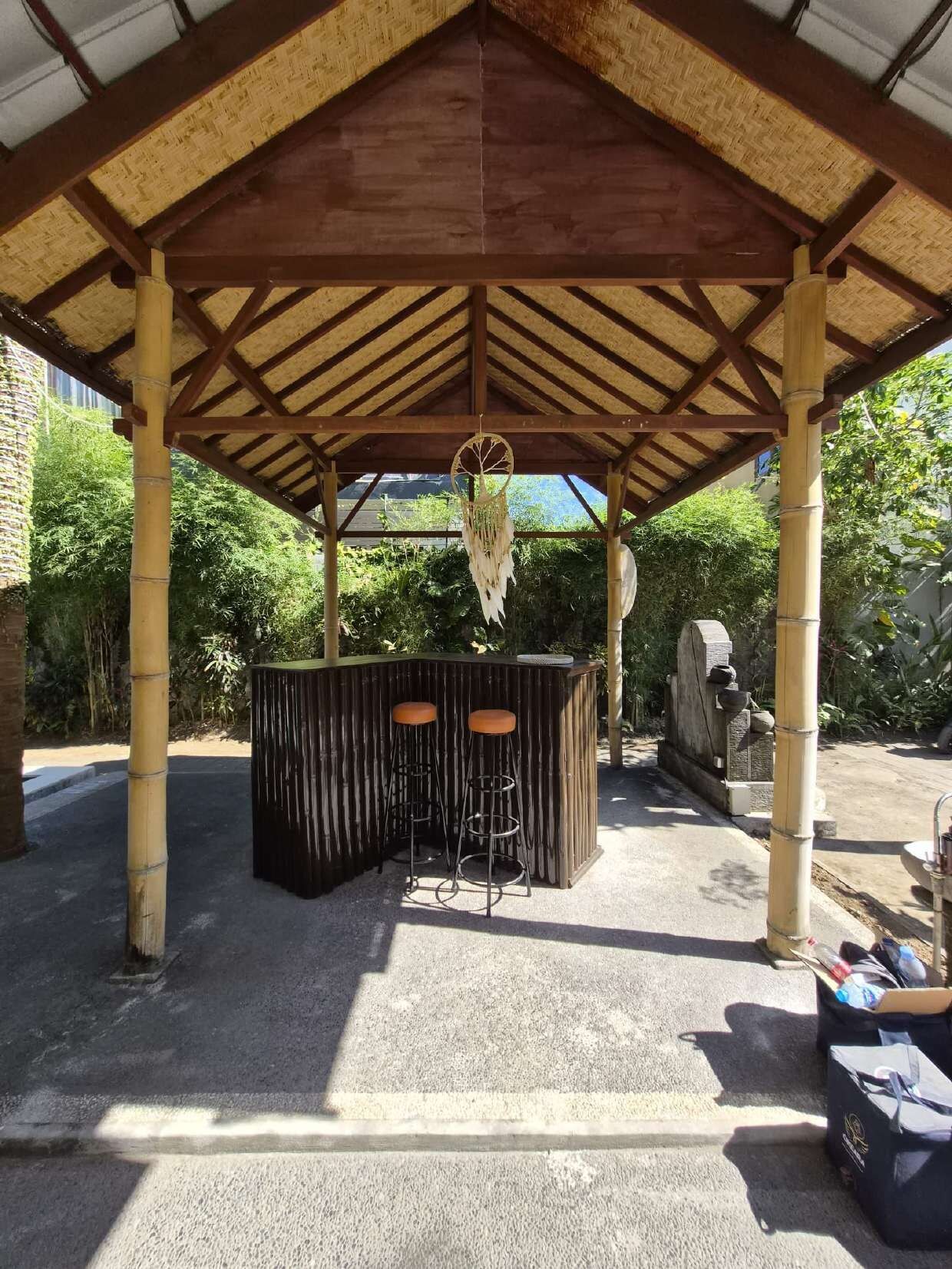 A covered outdoor area with a wooden structure, a bar with stools, and a decorative hanging item.