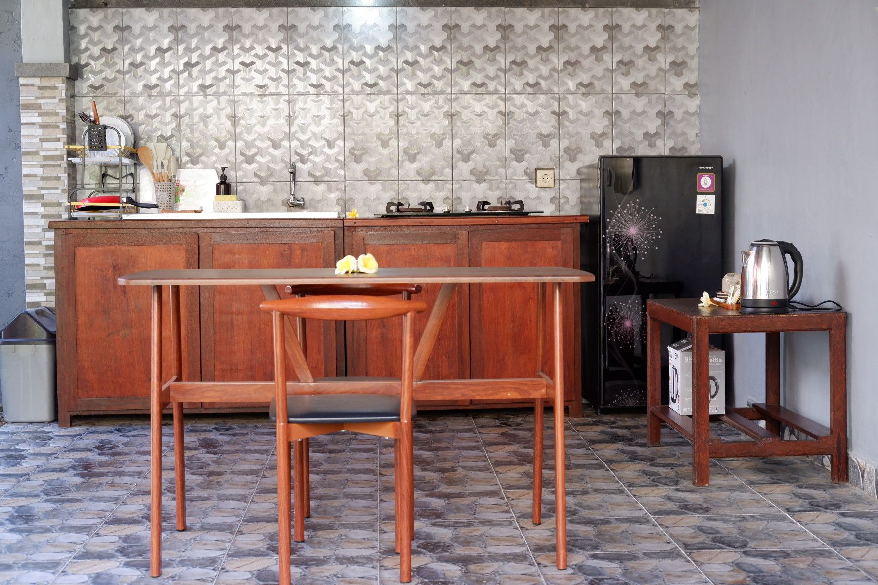 A kitchen with a wooden table and chairs, a refrigerator, and a kettle on a small table.