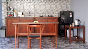 A kitchen with a wooden table and chairs, a refrigerator, and a kettle on a small table.