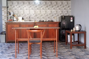 A kitchen with a wooden table and chairs, a refrigerator, and a kettle on a small table. - Lemon Blossom Guest House (Ubud)