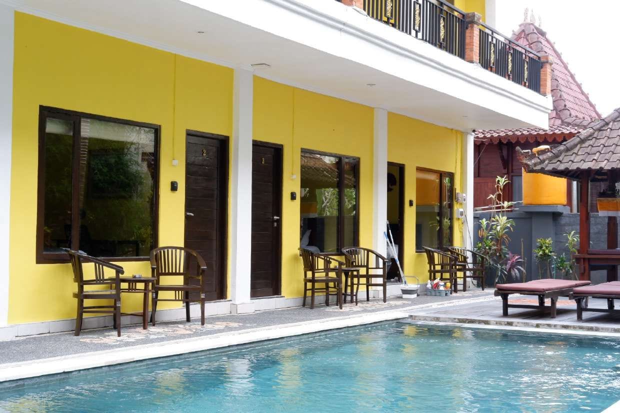 Un hôtel à la façade jaune, doté d’une piscine et d’un espace extérieur aménagé pour s’asseoir.